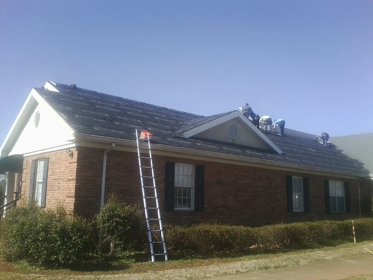 Crew tearing shingles off a brick ranch roof with a ladder set — Emergency Roof Repair work by our crew in South Lyme