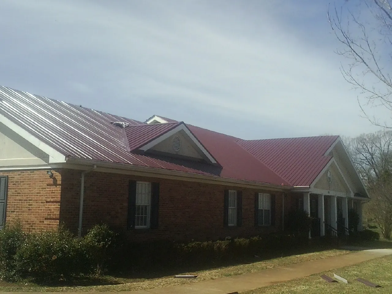 Red metal roof with gabled entries on a long brick building, from a Hail Damage Roof Repair job in South Lyme