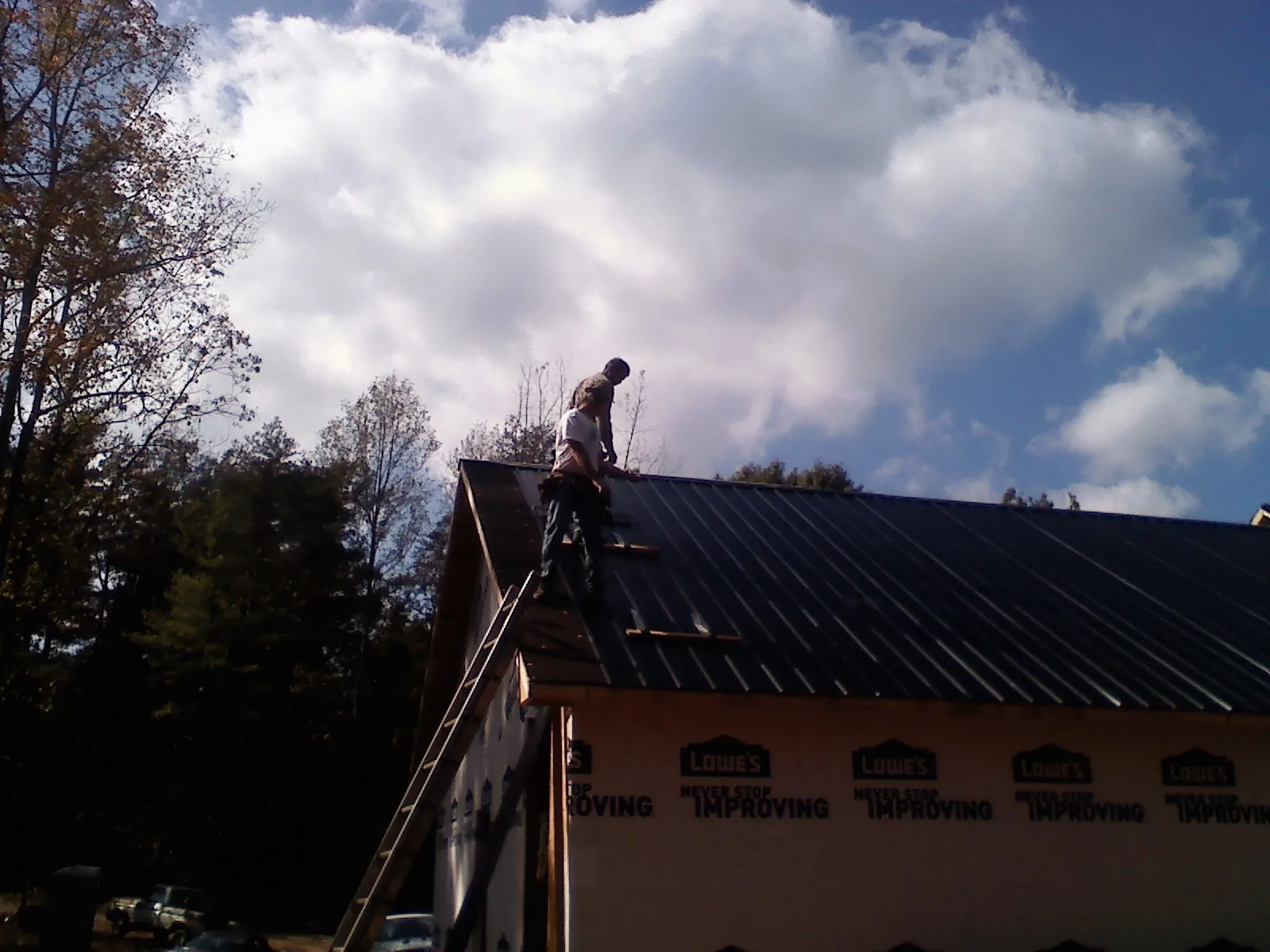 Roofer fastening dark metal panels high against a cloudy sky, from a Roof Inspection job in South Lyme
