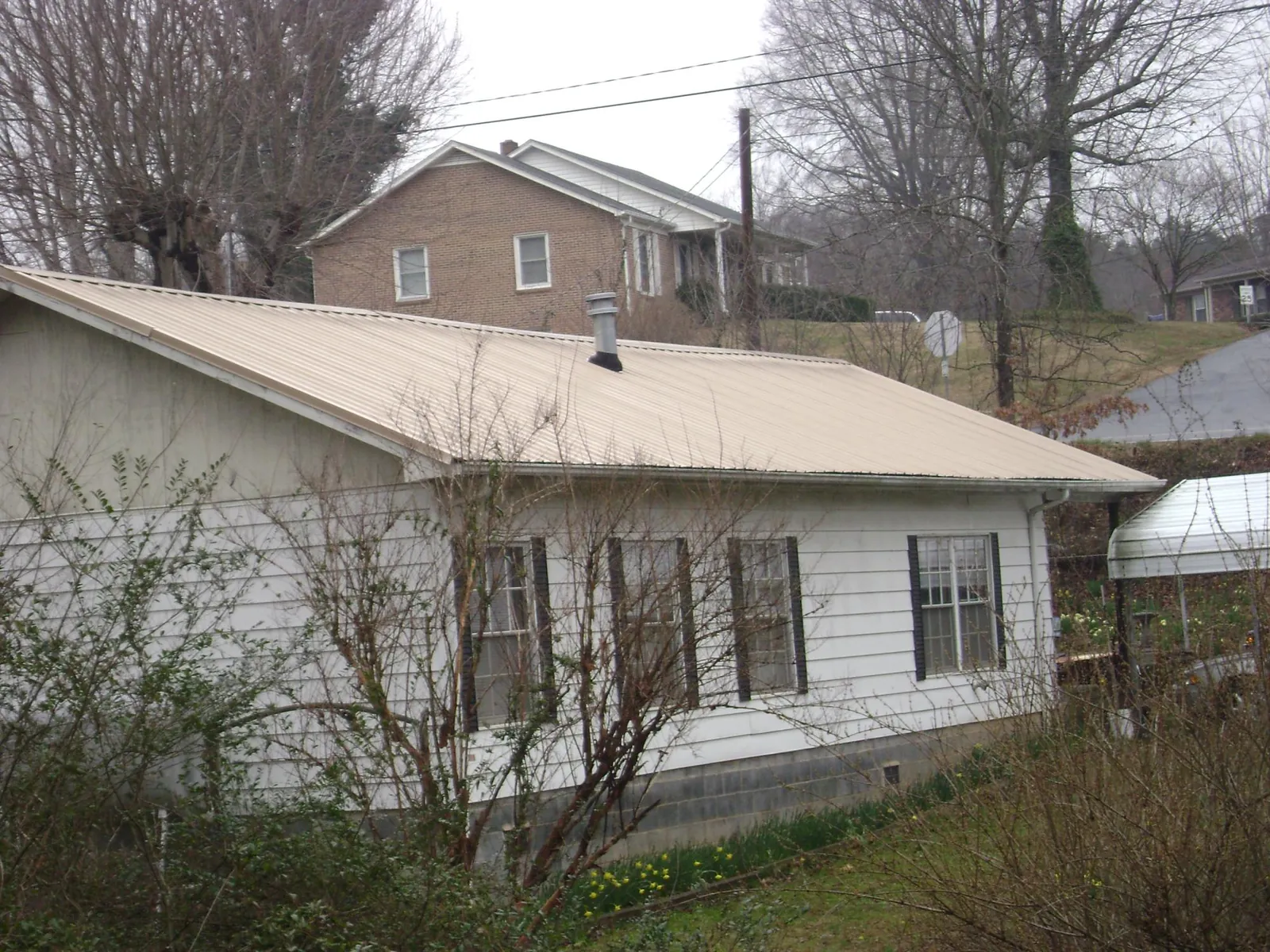Tan metal roof on a white sided house set into a hillside — Commercial Roofing by Roofing Brothers in South Lyme